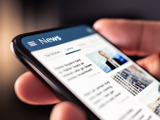 Close-up of a person holding a cell phone with a listing of news articles on screen