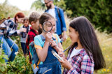 Children outdoor at a summer camp on a geo caching hunt holding a magnifying glass and clip board