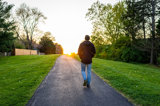 Silhouette of man walking towards sunset along paved path in spring.