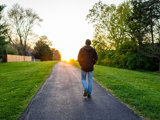 Silhouette of man walking towards sunset along paved path in spring.