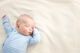 Baby in blue jumper sleeping on a white blanket.