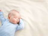 Baby in blue jumper sleeping on a white blanket.