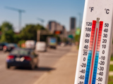 Close-up of a thermometer with a street and cars blurred out in the background.