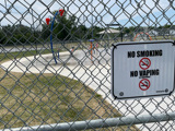 No Smoking sign outside of splash pad with children playing in the background out of focus.