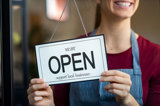 Woman holding 'Open - support local business' sign on the inside door.