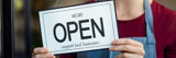 Woman holding 'Open - support local business' sign on the inside door.