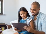 Dad reading to daughter on tablet smiling